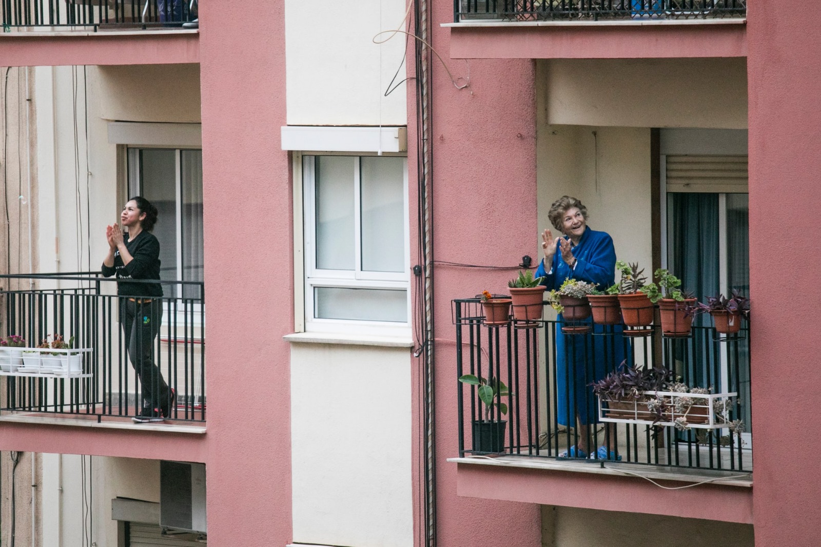 Twee mensen op hun eigen balkon. Ze klappen en kijken om zich heen.